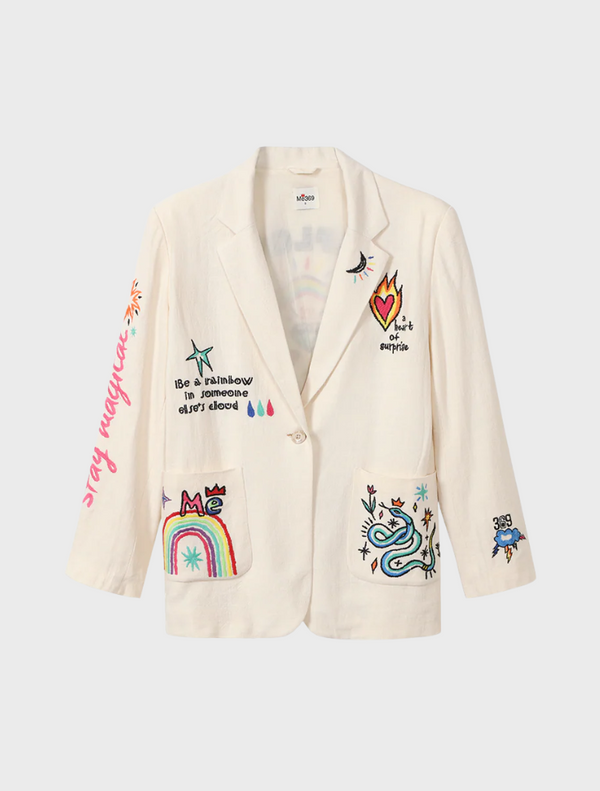 A woman models a white blazer adorned with elegant embroidered patterns.