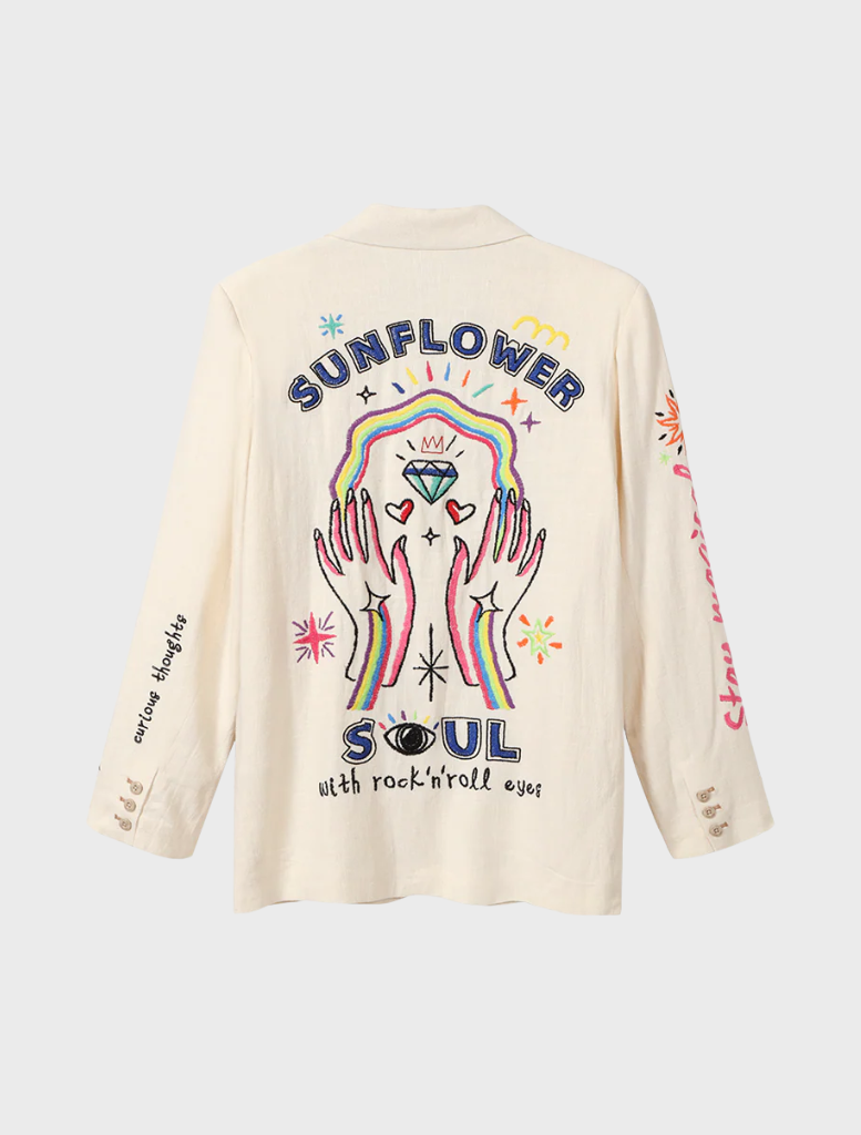 A woman showcases a white blazer with detailed embroidery, exuding style and sophistication.