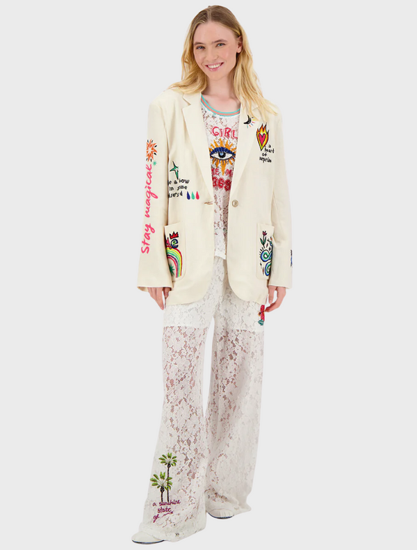 A woman in a white blazer featuring intricate embroidered designs stands confidently.