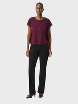 A woman in a purple top and black pants stands confidently, showcasing a stylish and modern outfit.