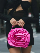 A woman in a black dress holds a fuchsia Rosita Rosette Frame Bag, showcasing its elegant design and vibrant color.