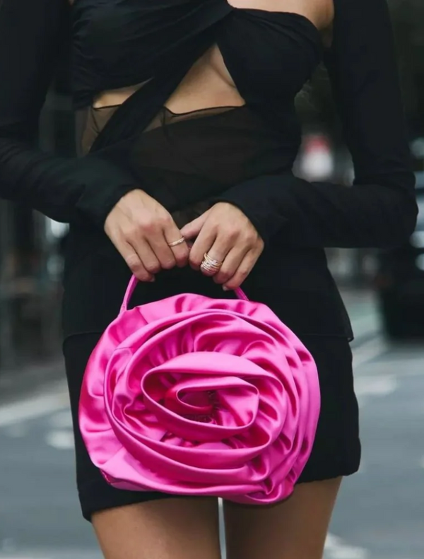 A woman in a black dress holds a fuchsia Rosita Rosette Frame Bag, showcasing its elegant design and vibrant color.