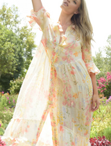 A woman in a floral dress walks through a garden, surrounded by a variety of colorful flowers and greenery.