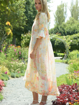 A woman wearing a floral dress walks gracefully through a lush garden, surrounded by colorful blossoms.