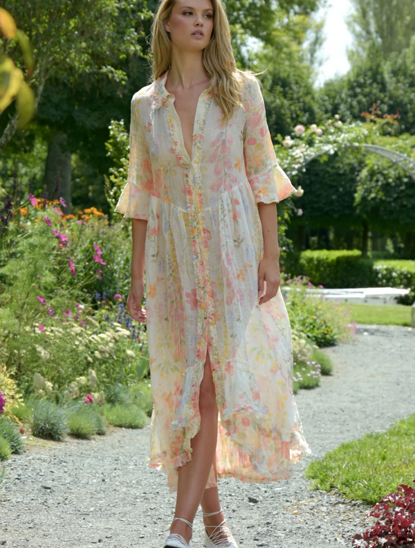 A woman in a vintage floral dress strolls through a vibrant garden filled with blooming flowers.
