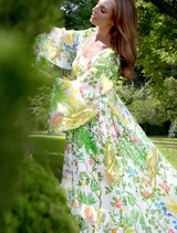 A woman wearing a floral dress walks leisurely in a park, enjoying the natural scenery around her.
