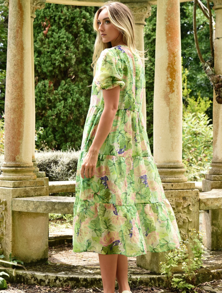 A woman wearing a green dress poses in front of a stone archway, highlighting her elegance against the historic backdrop.