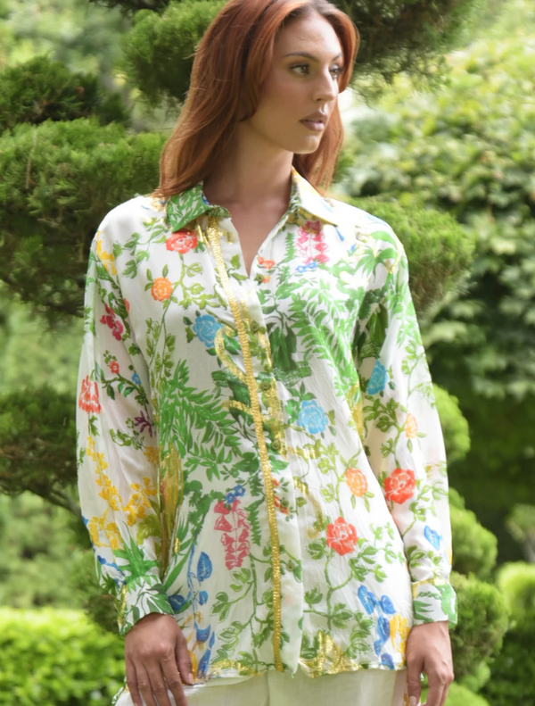 A woman in a floral shirt strolls through a park, surrounded by greenery and blooming flowers.