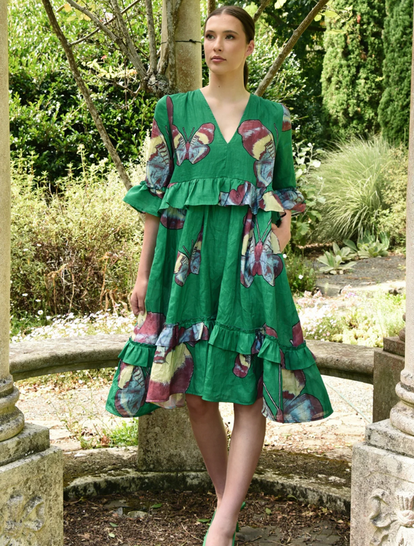 A woman wearing a green dress is seated on a bench, surrounded by a peaceful environment.