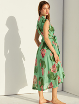 A green linen dress displayed on a hanger, featuring a relaxed fit and minimalistic style, set against a plain backdrop.