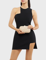 A woman wearing a black dress poses with a natural Haven Woven Clutch in her hand.