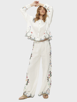 White linen shirt with floral embroidery, featuring dramatic sleeves and a scalloped hem, blending modern and heirloom styles.