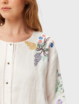 Helena shirt in pure white linen, featuring delicate floral embroidery, bohemian sleeves, and a scalloped hem for a romantic touch.