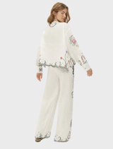 Elegant white linen shirt adorned with intricate floral embroidery, dramatic sleeves, and a scalloped hem, showcasing vintage inspiration.