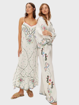 White linen shirt with antique-inspired floral embroidery, dramatic sleeves, and scalloped hem, merging modern design with tradition.
