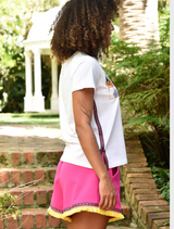 A woman wearing pink shorts and sneakers stands on a balcony, striking a pose against a sunny backdrop.