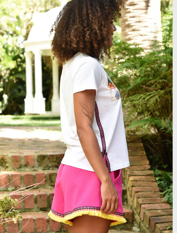 A woman wearing pink shorts and sneakers stands on a balcony, striking a pose against a sunny backdrop.