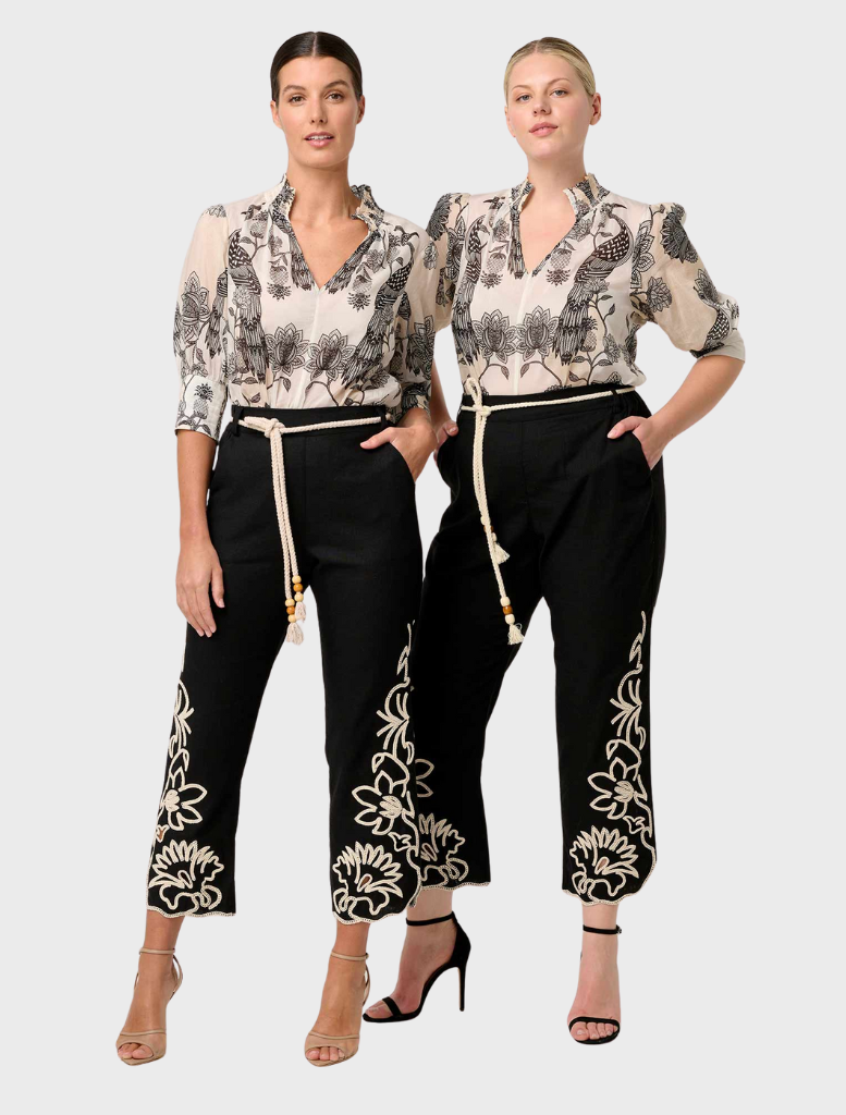 Two women wearing black and white floral print pants, showcasing the Oleander Placement Print Cotton Silk Blouse in Imperial Stone.