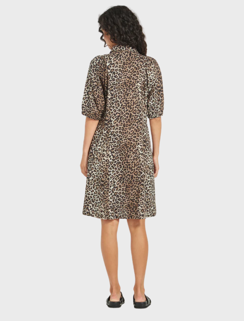 A woman dressed in a leopard print shirt and sunglasses, showcasing a trendy look with a relaxed expression.