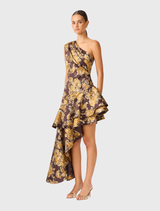Asymmetrical brown and gold floral midi dress with one-shoulder style, soft tuck detailing, and a flowing high-low hem.