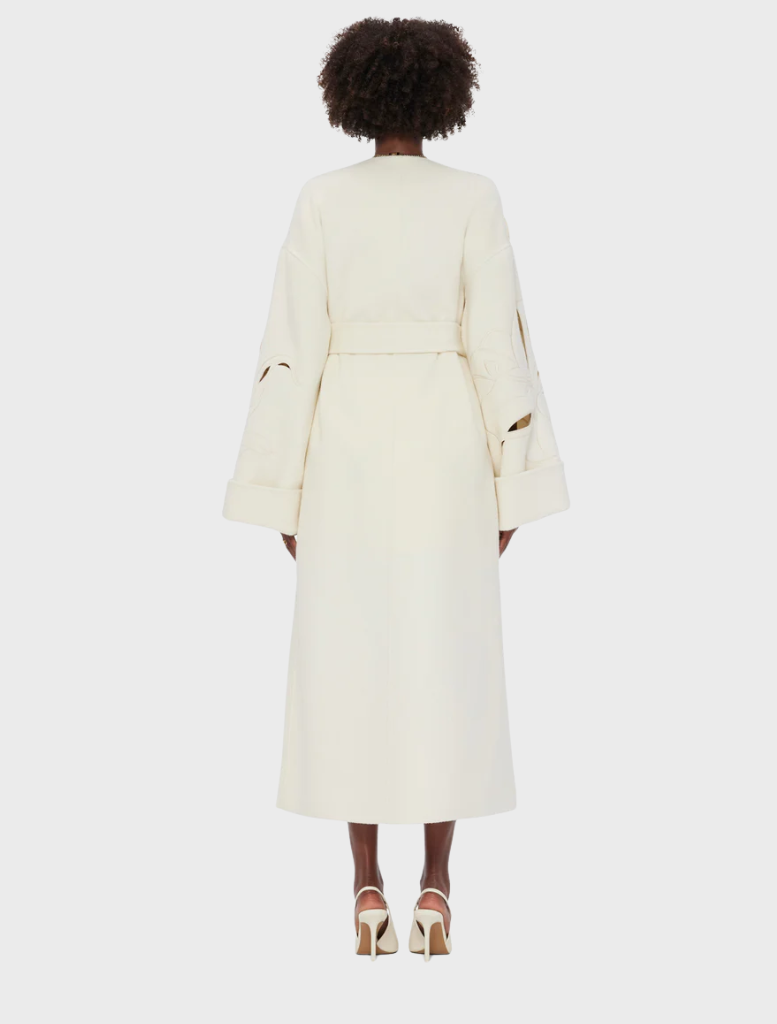 A woman seen from behind, wearing a white coat, with her hair cascading down her back.