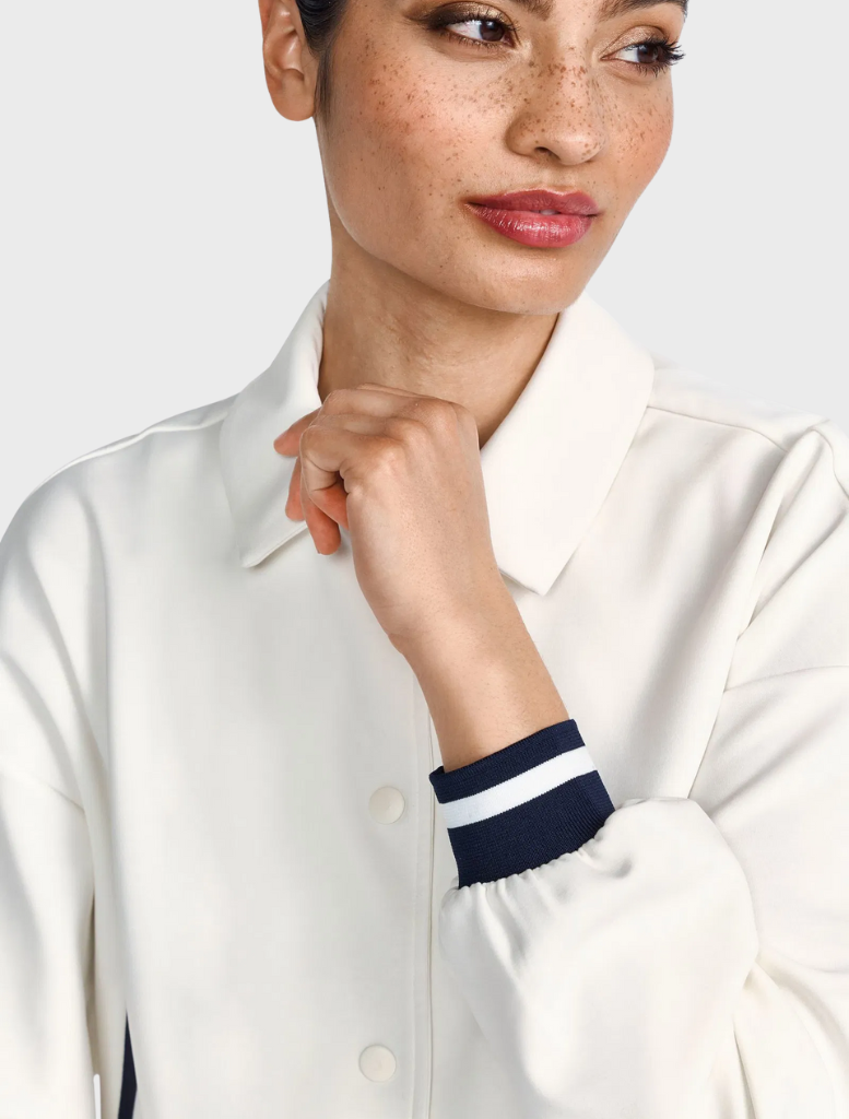 A woman in a white shirt and black jacket stands confidently, showcasing a professional appearance.