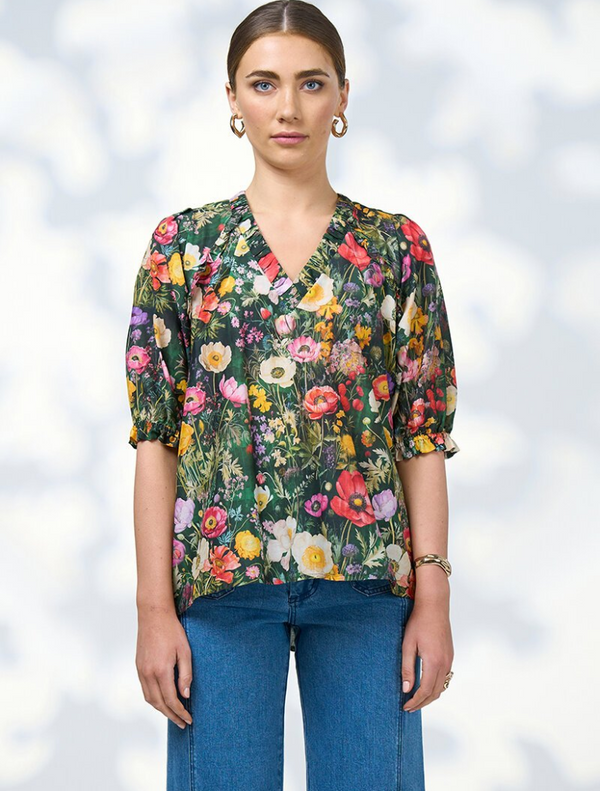 A model displays a floral blouse paired with wide-leg pants, highlighting the Looking Glass Top in Ivy Multi.
