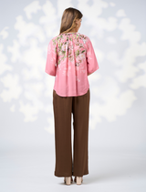  woman dressed in a pink top and brown pants stands, exuding a cheerful demeanor.