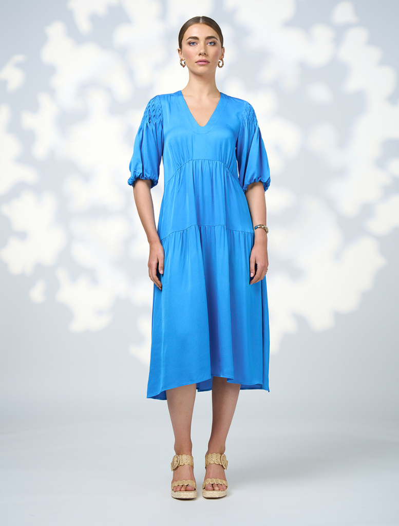 A model showcases a blue v-neck dress from Genf Gilet - Candy, highlighting its elegant design and flattering silhouette.