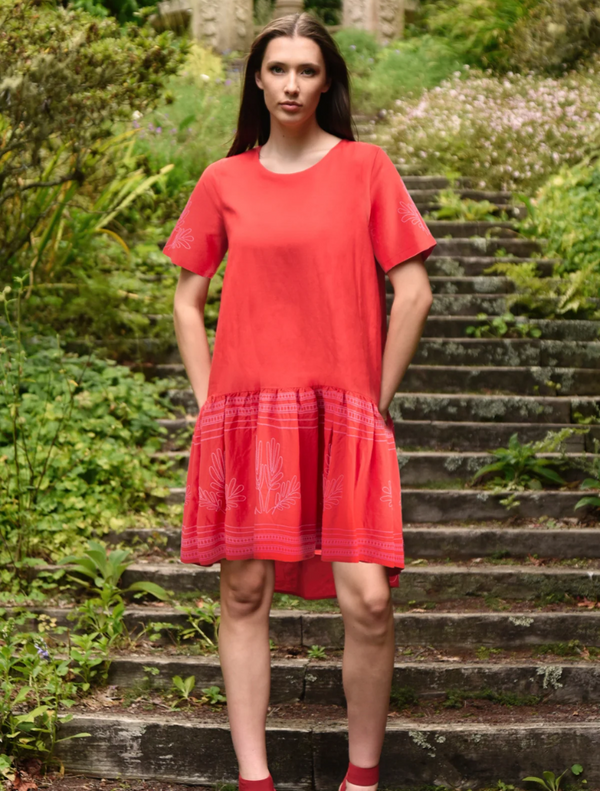 A woman in a red dress stands confidently on a set of steps, showcasing her elegant pose and vibrant attire.