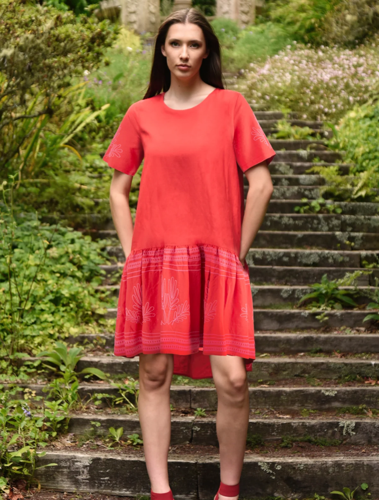 A woman in a red dress stands confidently on a set of steps, showcasing her elegant pose and vibrant attire.
