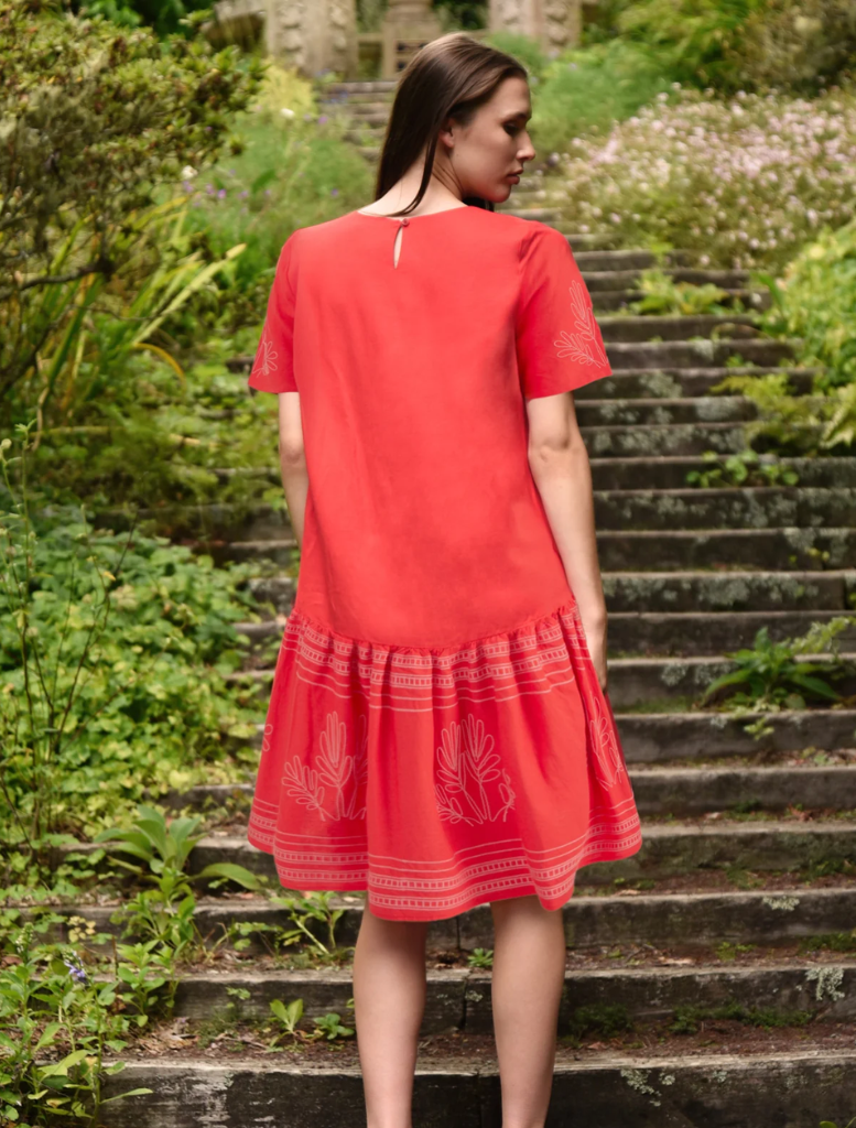 A woman in a flowing red dress stands on steps, highlighting her elegance and the vivid color of her outfit.