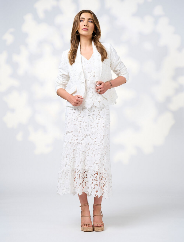 A woman dressed in a white silk jacket and pants poses elegantly, highlighting her fashionable ensemble.