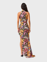 Back view of a woman in an orange floral print Kiran Halter Gown, showcasing the vibrant design and flowing silhouette.
