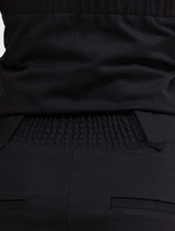 Back view of a man dressed in a black shirt and black pants, standing upright.