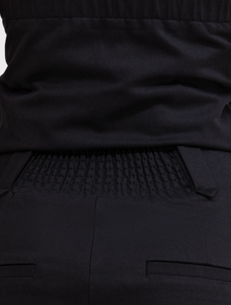 Back view of a man dressed in a black shirt and black pants, standing upright.