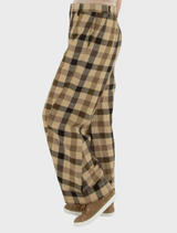 A woman in plaid trousers and a white shirt stands, showcasing a stylish outfit.