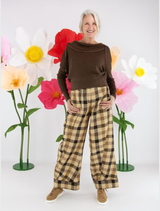 A woman wearing brown plaid trousers stands in front of colorful flowers, showcasing a stylish outdoor look.
