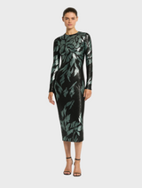 A woman in a stylish black dress with green leaf designs, representing the Larissa Midi Dress in Mint Black.