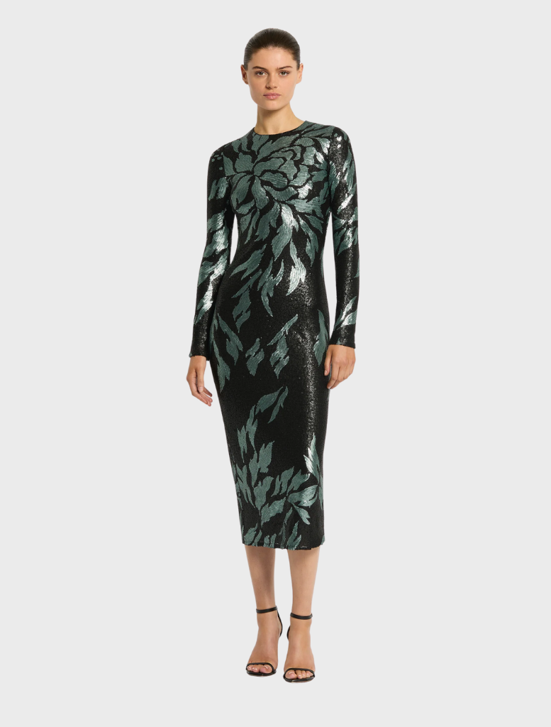 A woman in a stylish black dress with green leaf designs, representing the Larissa Midi Dress in Mint Black.