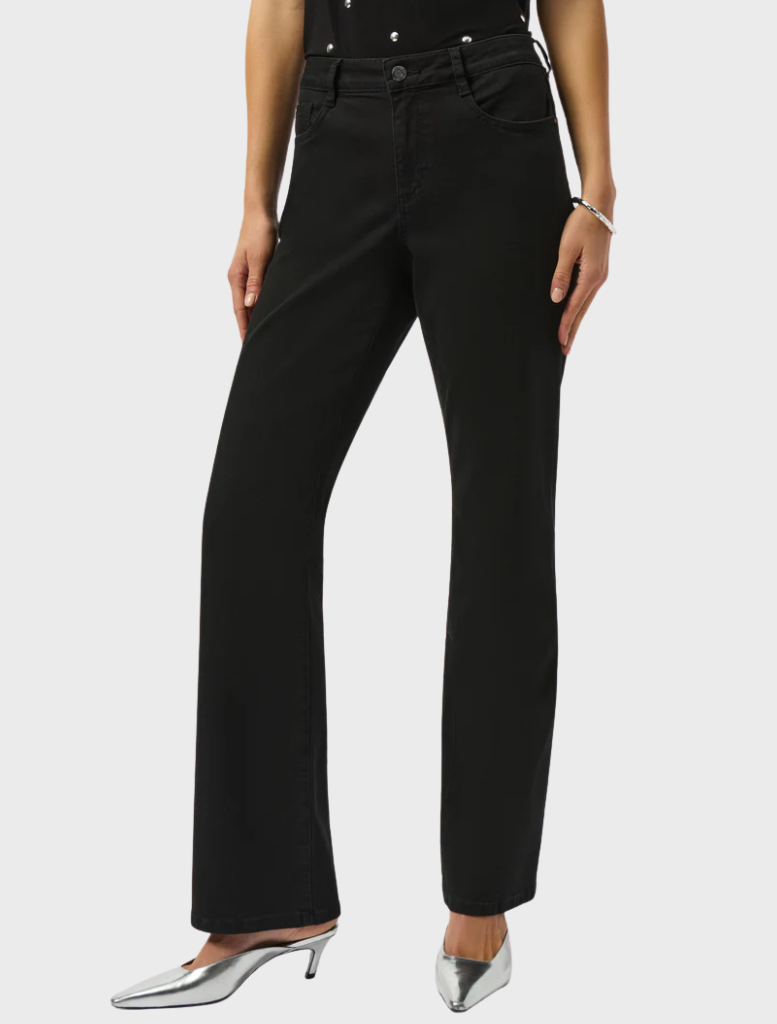 A woman wearing black trousers and a stylish top stands, presenting a polished and fashionable look.