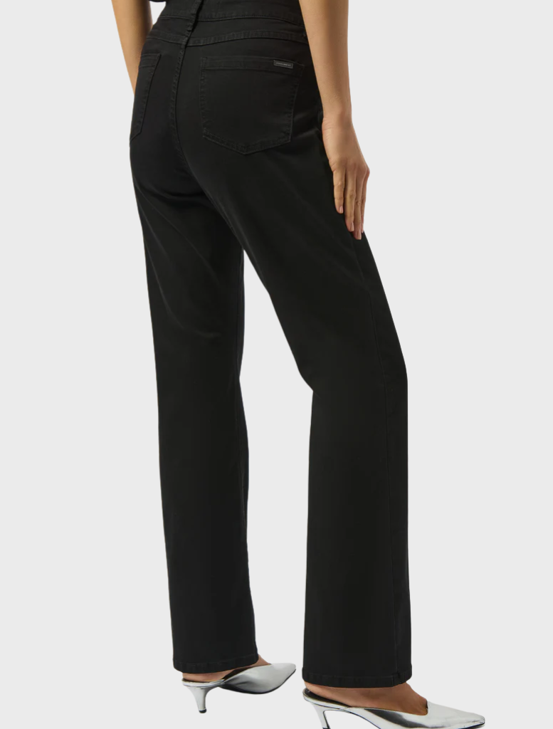 A woman in black pants and a fitted top stands, exuding a chic and contemporary style.