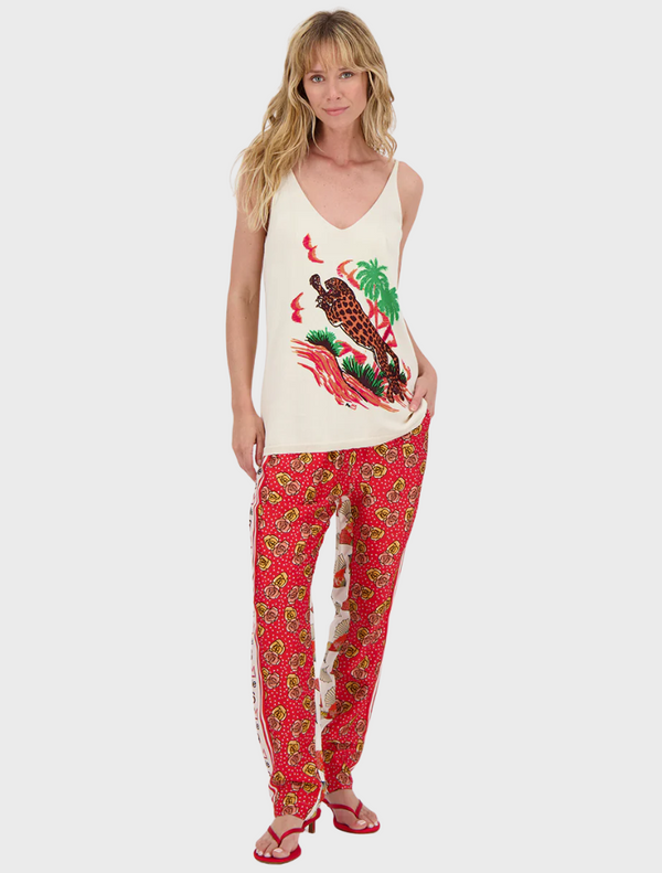 A woman in a white tank top and red pants stands confidently, showcasing her casual yet stylish outfit.