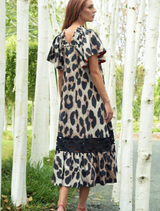 A woman wearing a leopard print dress poses in front of vibrant trees, highlighting her fashionable choice.