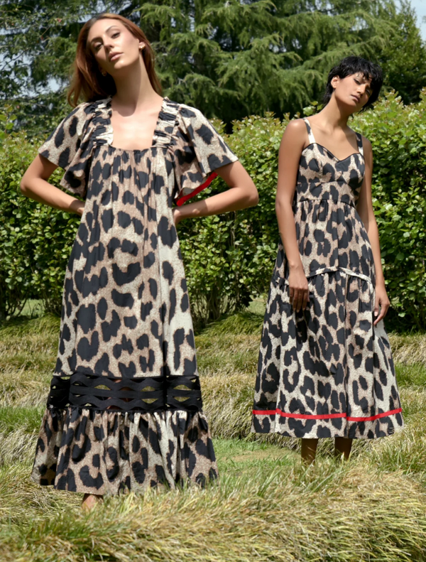 A two woman wearing a leopard print dress poses in front of trees, highlighting her fashionable choice in a natural setting.
