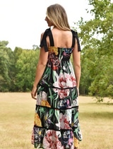 A woman wears a stylish floral print dress adorned with an array of colorful blooms on a soft fabric.