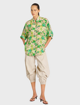 A model displays a floral shirt in green and yellow, characterized by its bright and cheerful pattern.
