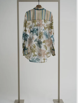 A tropical print blouse in lime multi colors is hanging on a display stand.