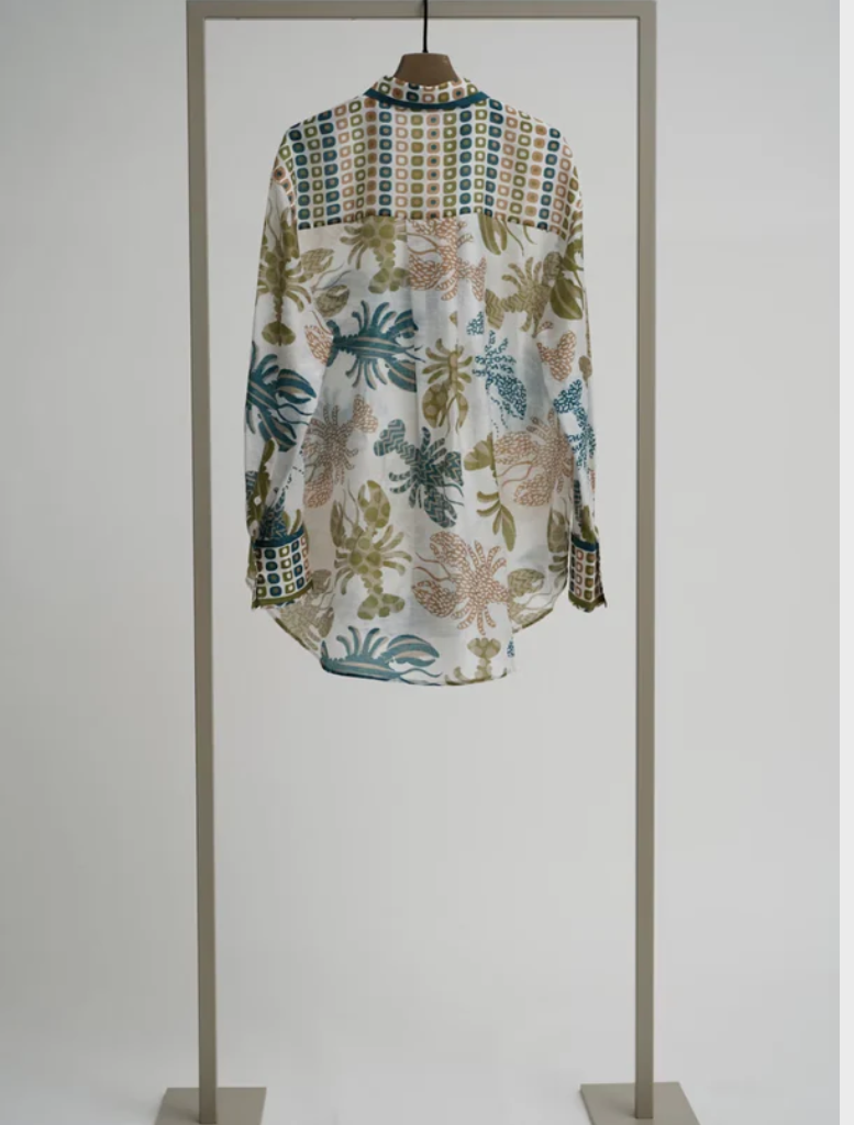 A tropical print blouse in lime multi colors is hanging on a display stand.