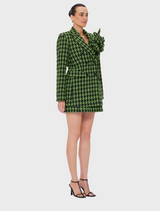 A woman wearing a green and black checkered blazer dress, standing confidently with a neutral background.